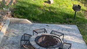 Un patio de concreto con un hogar circular y sillas de metal alrededor.
