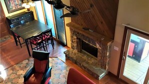 Ein gemütlicher Wohnbereich mit Kamin aus Stein, einem Esstisch mit Stühlen und einem roten Sofa.