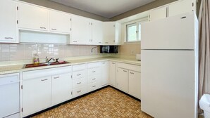 Una cocina compacta con armarios blancos, un microondas, un refrigerador y piso de baldosas.