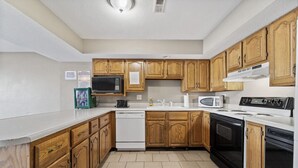 Una cocina con armarios de madera, microondas, lavavajillas, estufa y fregadero.