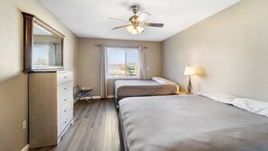 Habitación de hotel con dos camas, un ventilador de techo, un aparador, una ventana con cortinas y una lámpara.