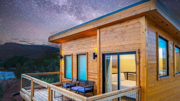 Una cabaña de madera con balcón, cama y ventana con vistas al paisaje.