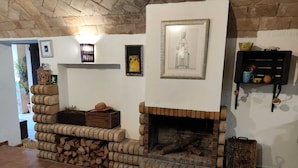 Un intérieur rustique avec une cheminée en briques, une pile de bois de chauffage et divers tableaux encadrés accrochés aux murs.