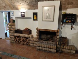 Un interior rústico con chimenea de ladrillo, leña apilada y varias obras de arte enmarcadas en las paredes.