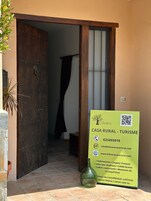 Una puerta de madera rústica da paso a una habitación con un ventanal grande y un letrero que anuncia una casa rural para turismo.