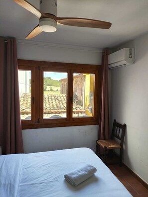 A bedroom with a bed, a wooden chair, a ceiling fan, and a window with curtains.