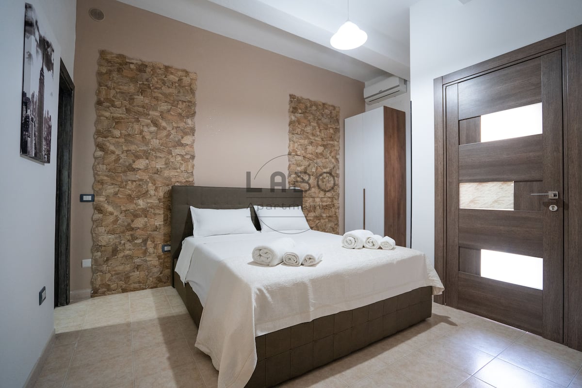 A bedroom with a stone accent wall, a bed with neatly folded towels, and a wooden door with a window.