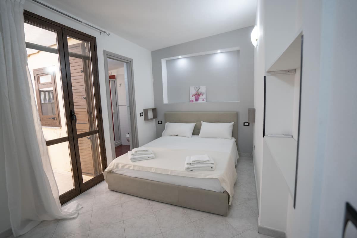 A bedroom with a bed, a sliding glass door, a white wall, and a small painting.
