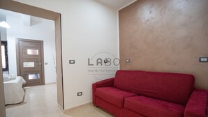 A red sofa in a room with a white door and a wall with a logo. - Ammos Guest House (Tropea)