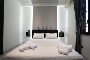 A hotel room with a bed, two bedside tables, a wall-mounted air conditioner, and a window with curtains. - Ammos Guest House (Tropea)