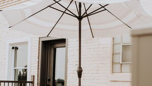 An outdoor patio with a wooden table and chairs, a white umbrella, and a brick wall. - Charming renovated guesthaus in the heart of Historic Hermann. (Hermann)