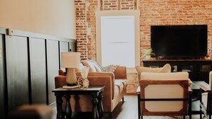 A living room with a brick wall, a sofa, a coffee table, and a television. - Charming renovated guesthaus in the heart of Historic Hermann. (Hermann)