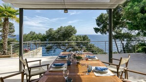 A wooden dining table set for four with blue napkins and glasses, overlooking a pool and the sea. - Sea Views. 5 Min Walk to Beach. Pool (Llafranc)