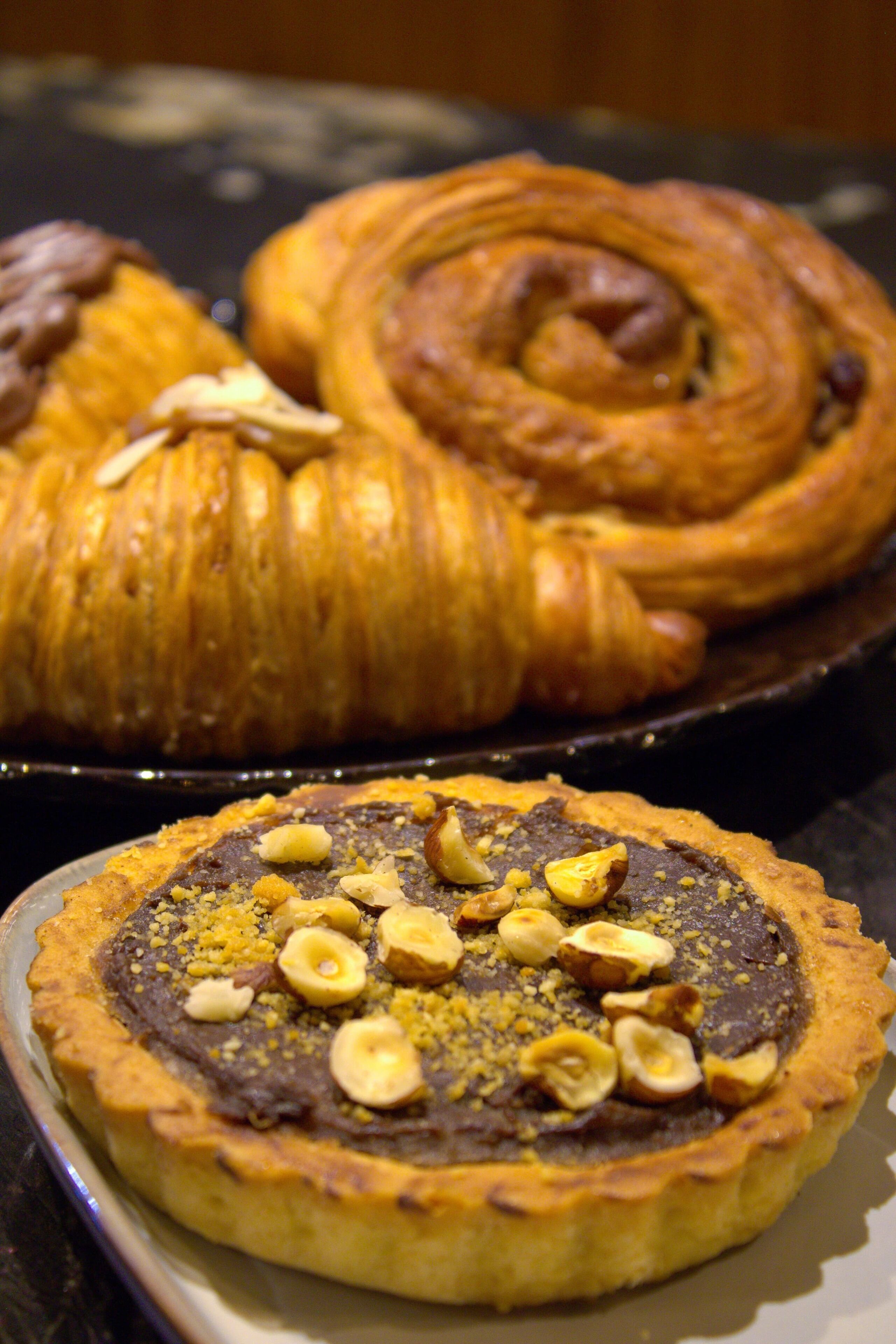 A dessert plate with a chocolate tart topped with nuts and a pastry case in the background.