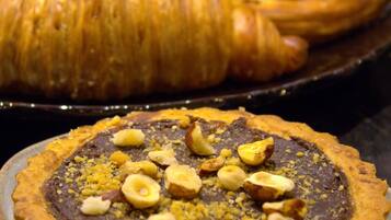 A dessert plate with a chocolate tart topped with nuts and a pastry case in the background.