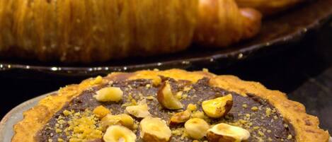 A dessert plate with a chocolate tart topped with nuts and a pastry case in the background.