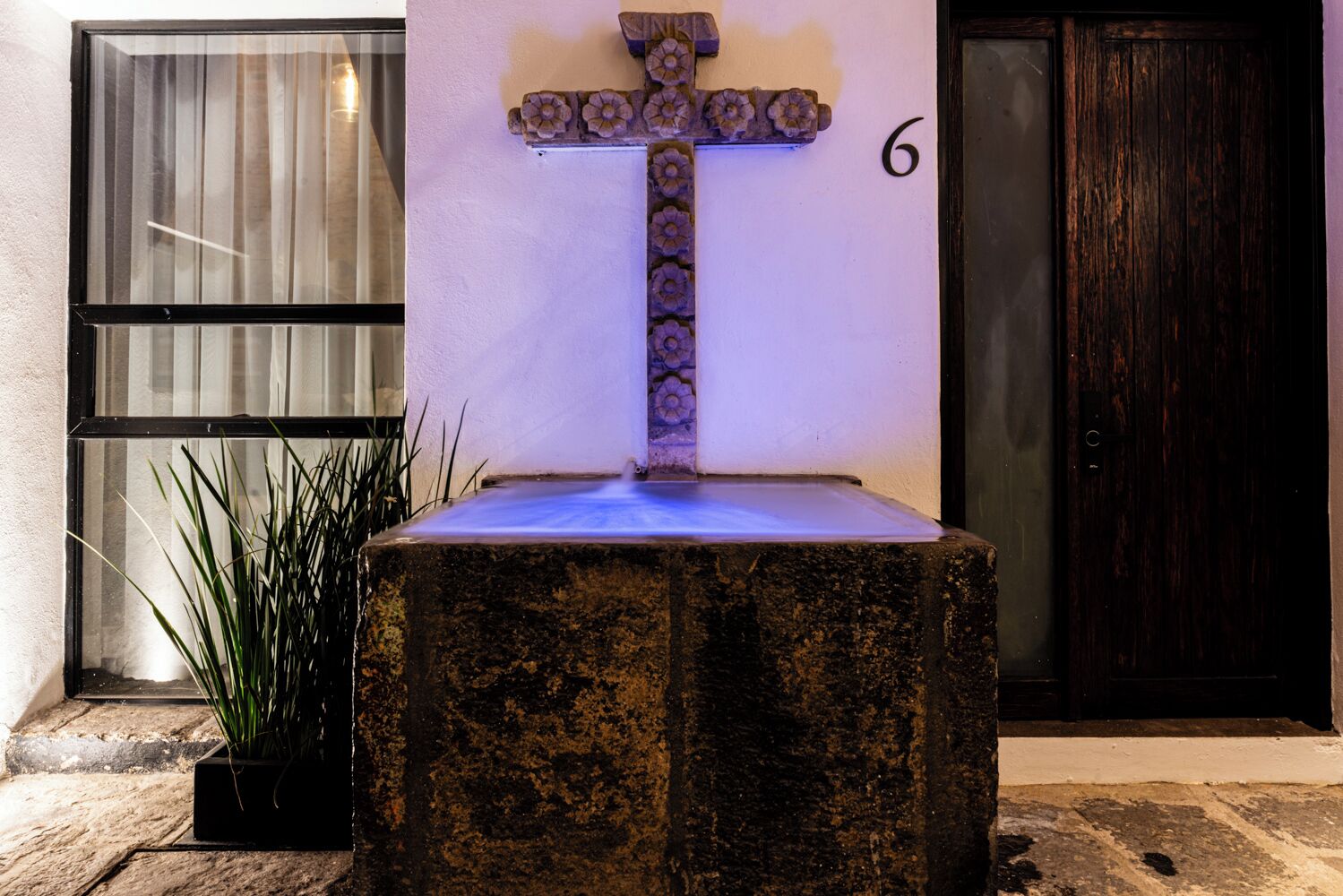 A stone cross with a blue light on top, a potted plant, and a door with the number 6.