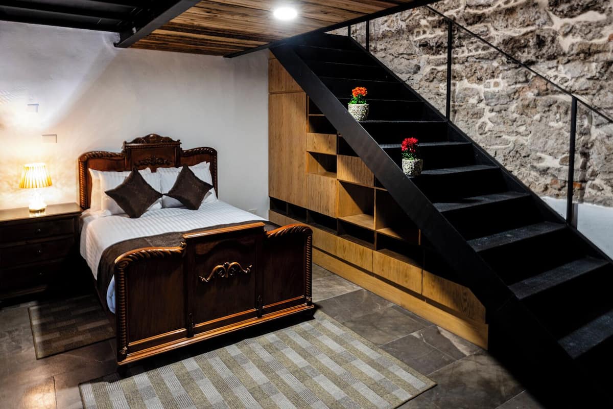 Ein Schlafzimmer mit einem hölzernen Bett, einem Nachttisch, einer Lampe, einer Steintreppe und einem kleinen Topfpflanzen.
