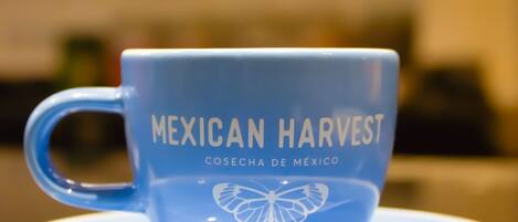 Uma xícara de café azul com a inscrição 'Mexican Harvest' e um desenho de borboleta em um pires.