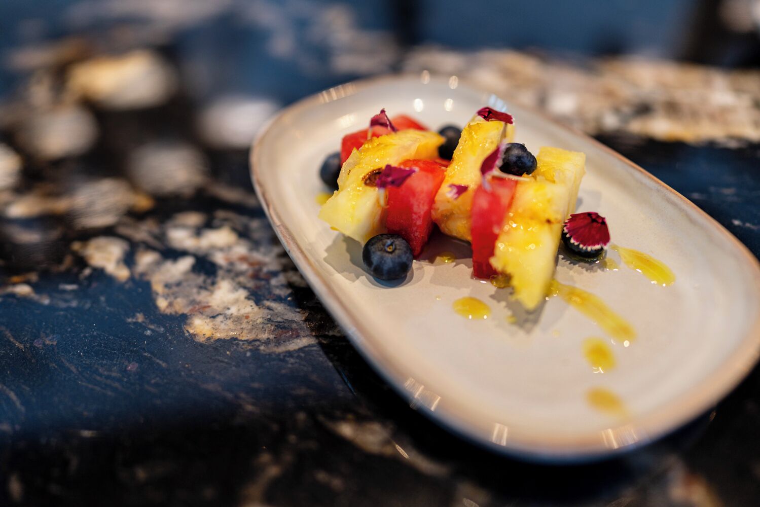 Een witte schaal met een fruitsalade op een donkere, geribbelde ondergrond.