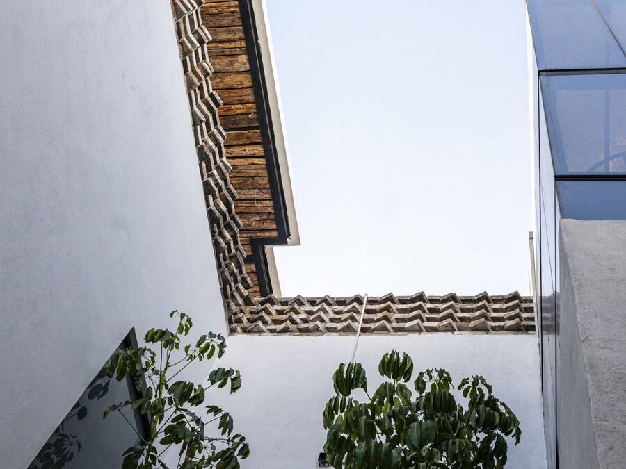 A corner view of a building with a white wall, a wooden decorative element, and a plant.