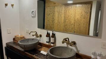 Un baño con dos lavamanos de piedra, un mueble de tocador de madera, un espejo grande y un armario de madera.