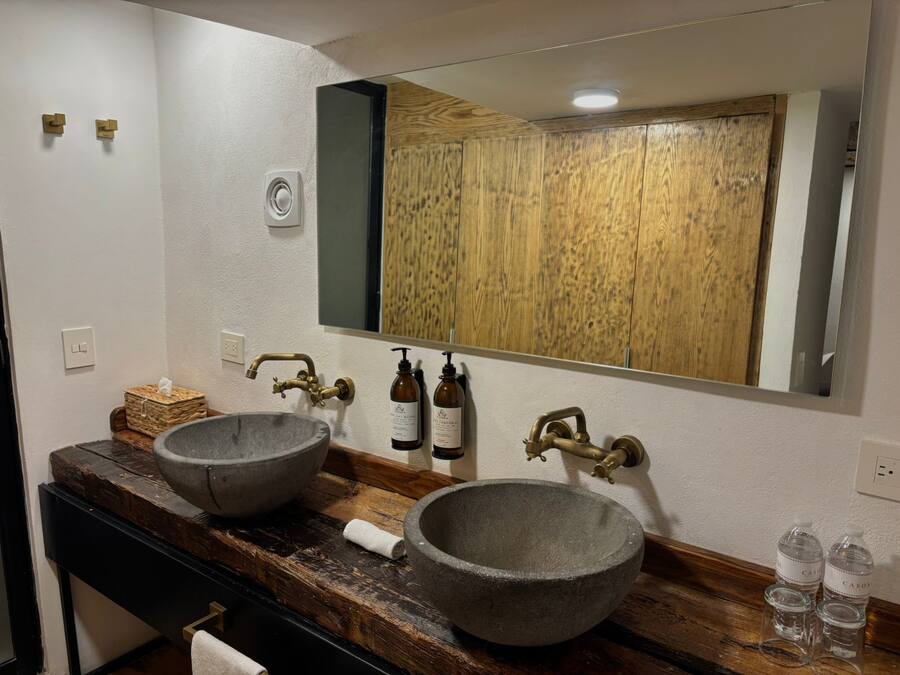 Un baño con dos lavamanos de piedra, un mueble de tocador de madera, un espejo grande y un armario de madera.