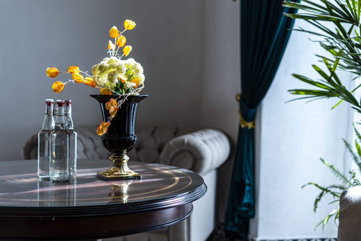 A round table with a black vase containing yellow flowers and a clear bottle.