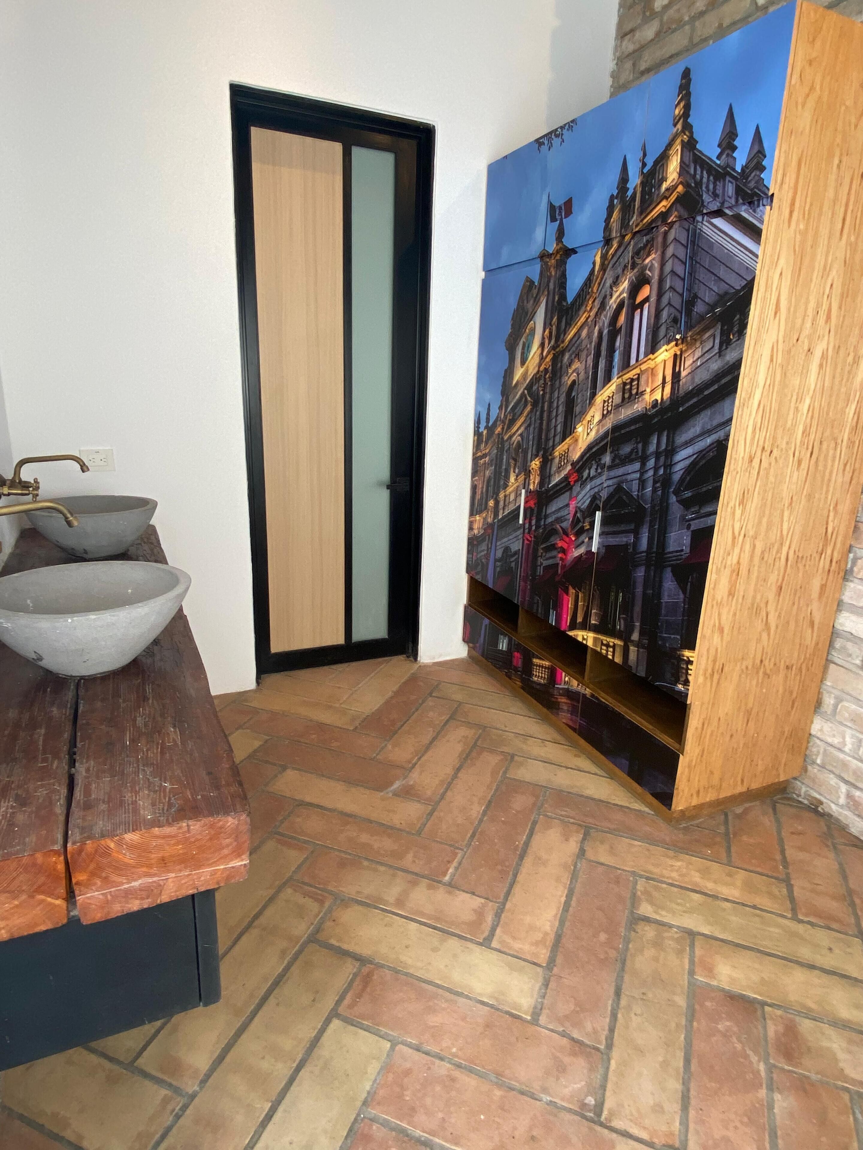 A room with a wooden table, a large painting of a building, a door, and a tiled floor.