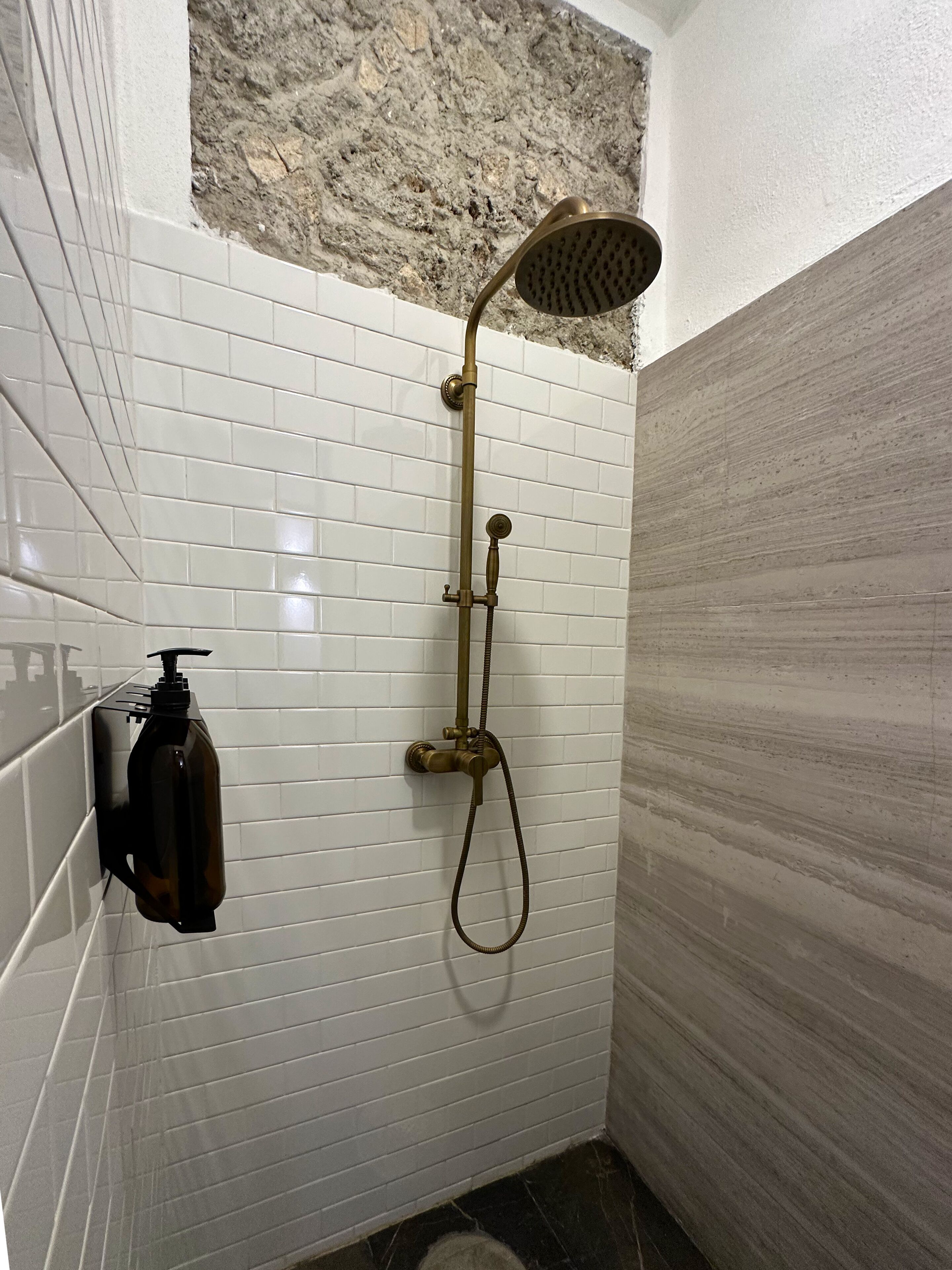 A shower with a handheld showerhead and a handheld shower attachment, mounted on a white tiled wall.
