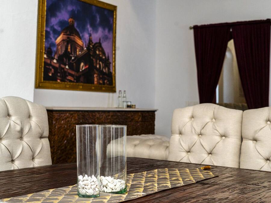 Un comedor con una mesa dispuesta para dos personas, que presenta un tablero de madera oscura, un camino de mesa estampado y dos jarrones altos de vidrio con guijarros blancos.