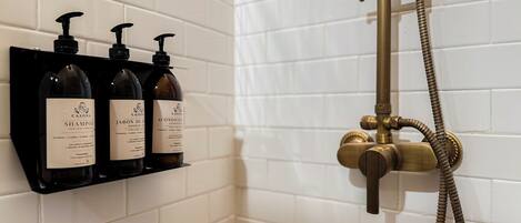 Un baño con paredes de azulejos blancos, un estante para dispensador de jabón negro y un cabezal de ducha de latón.