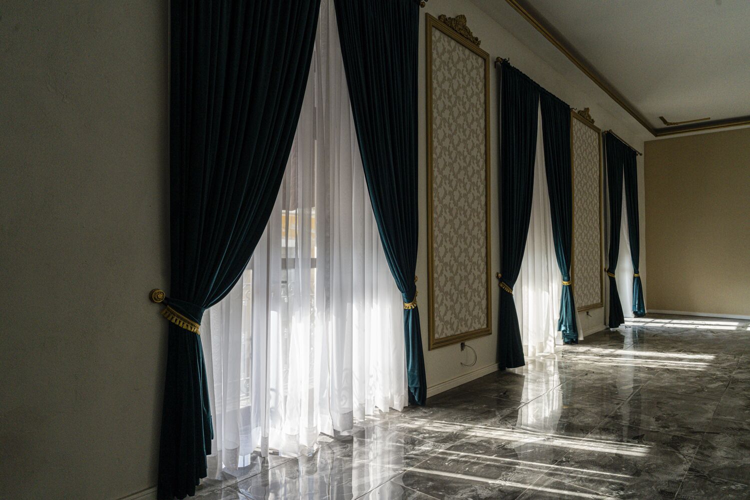 A hallway with dark blue curtains, a patterned wall, and a marble floor.