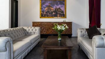 A living room with two tufted sofas, a dark wooden coffee table, and a painting of a building on the wall.