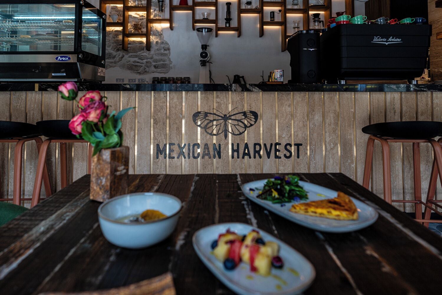 A restaurant interior with a wooden counter, a coffee machine, and a sign reading "MEXICAN HARVEST".