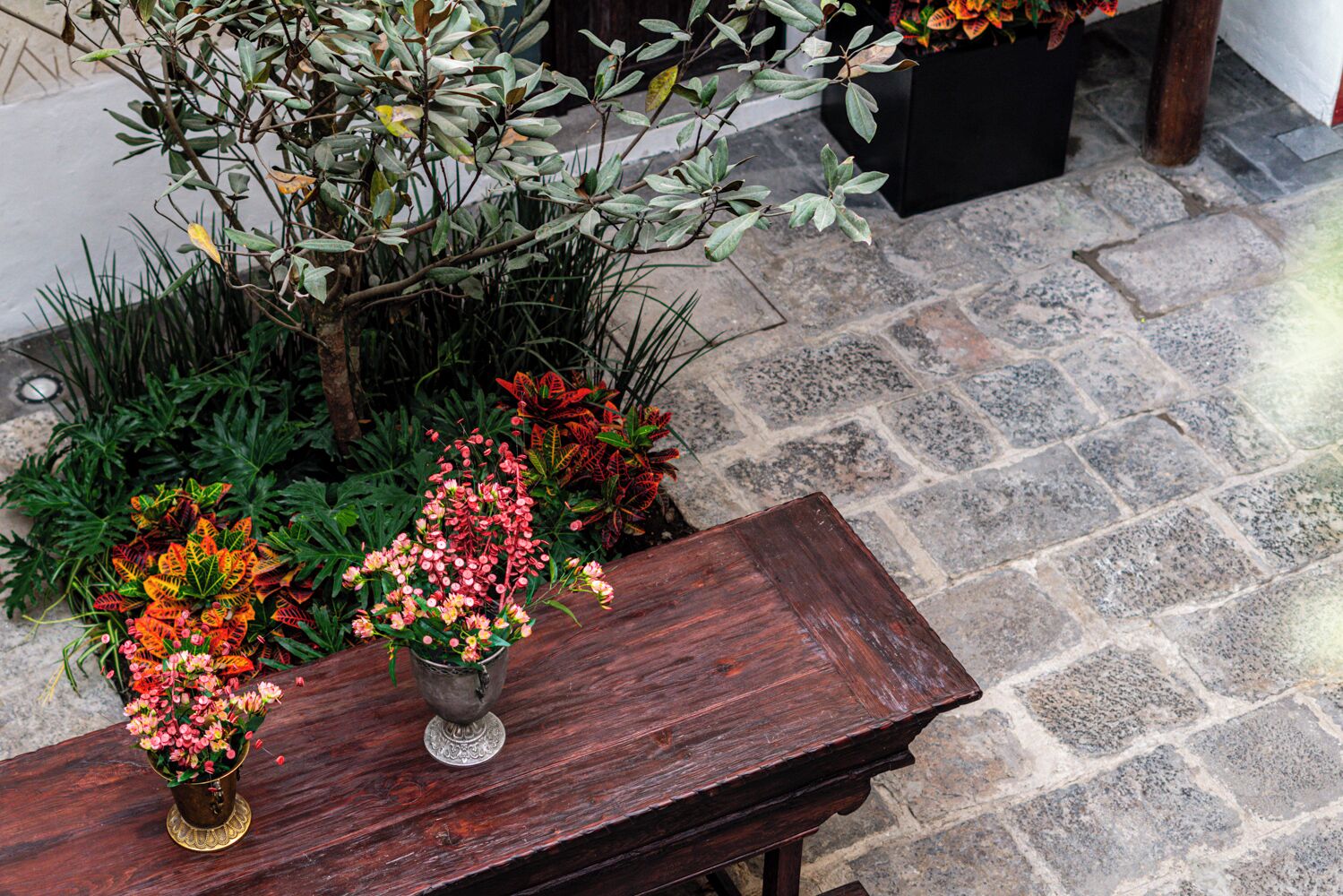 Une table en bois, un vase en métal et une plante en pot.