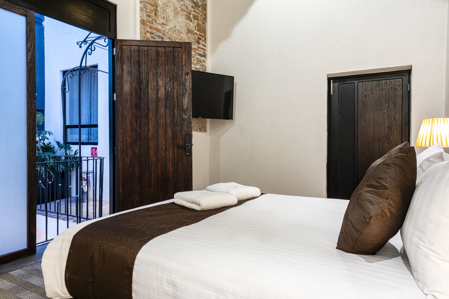Une chambre d’hôtel avec un grand lit, une armoire en bois, un téléviseur fixé au mur et un balcon agrémenté de plantes.