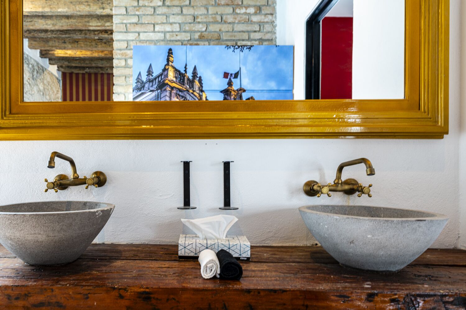Een badkamer met twee grote stenen wastafels, messing kranen en een spiegel met gouden lijst.