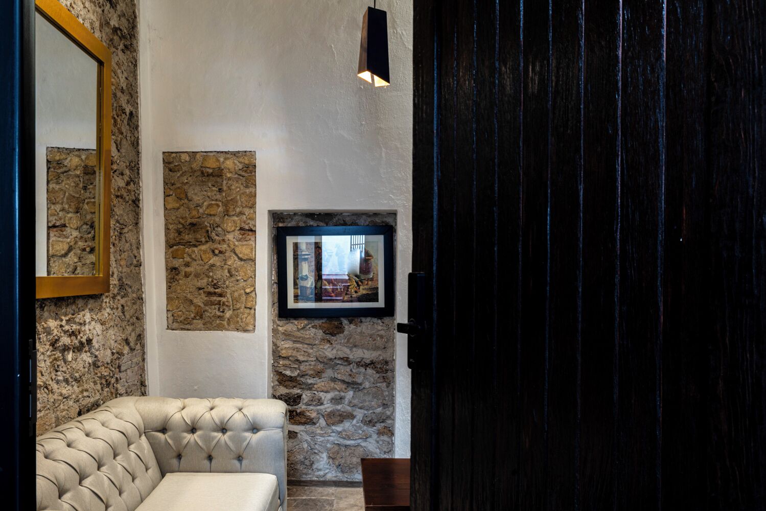 A room with a stone wall, a framed picture, a tufted sofa, and a dark wooden door.