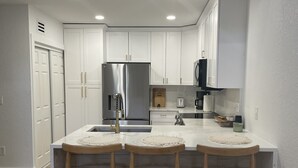 A modern kitchen with white cabinetry, a stainless steel refrigerator, a sink, and bar stools.