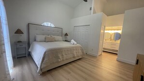 A bedroom with a large bed, a nightstand, a dresser, and a walk-in closet.