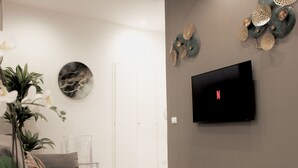 A modern living room with a grey sofa, a clear glass coffee table, a potted plant, and a flat-screen TV mounted on the wall. - Ponte Vecchio｜Tower of Gelfi (Firenze)