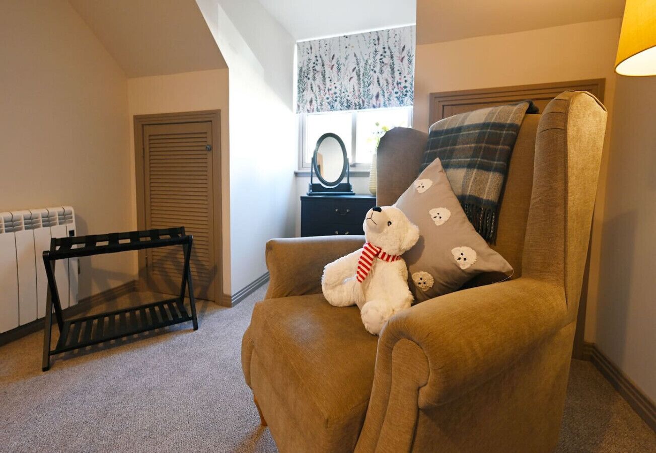 A cozy living room with a brown armchair, a teddy bear, and a plaid pillow.