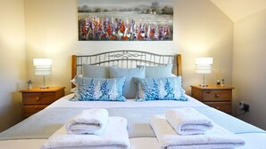 Una cama bien hecha con dos almohadas, dos mesitas de noche con lámparas y un cuadro sobre la cama.
