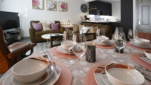 Un comedor con una mesa dispuesta para seis personas, rodeado de sofás y un televisor.