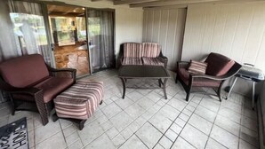 Un'area patio coperta con un divano, una poltrona e un poggiapiedi, una porta scorrevole in vetro che dà su uno spazio esterno e un tavolino.