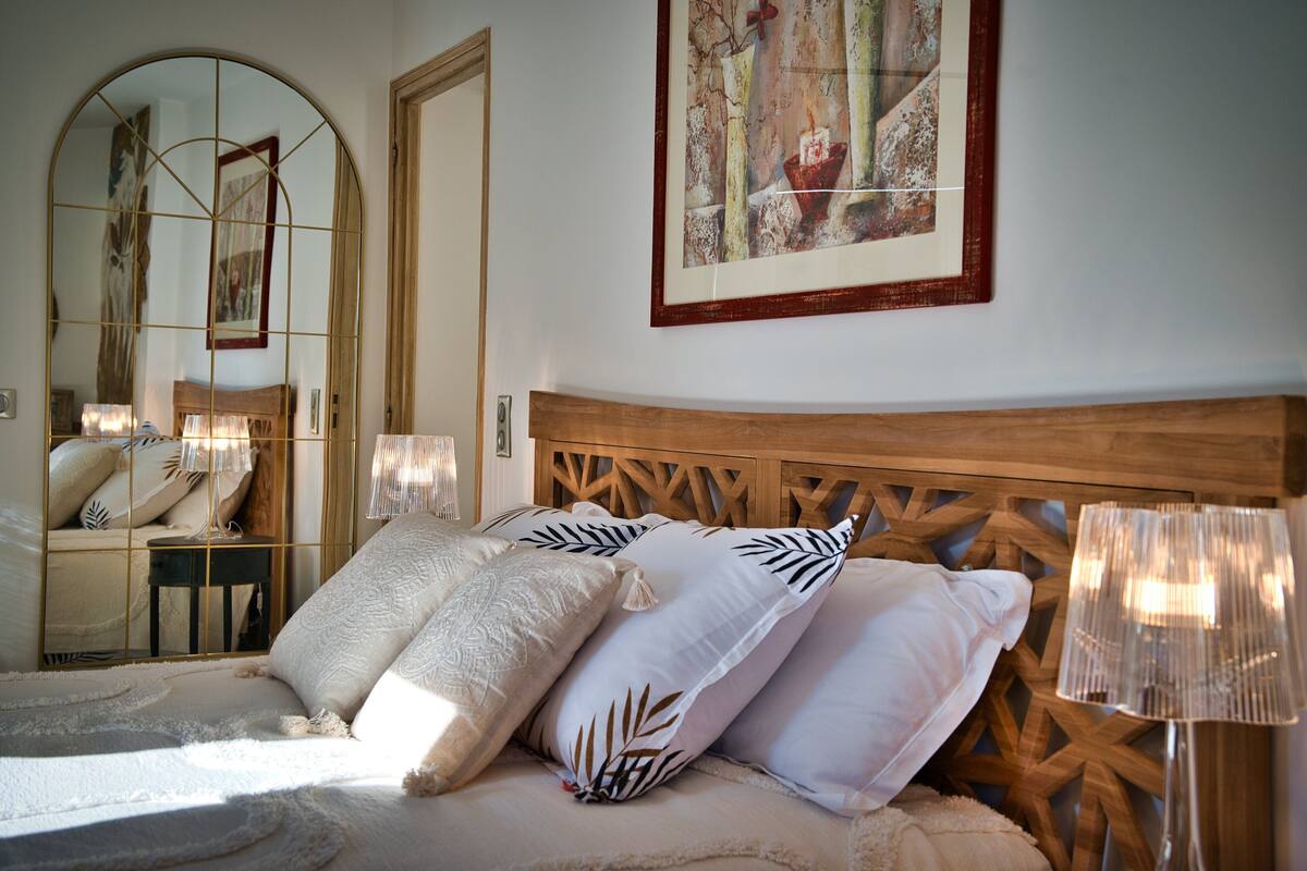 Quarto com cabeceira de madeira, um espelho grande e uma obra de arte emoldurada na parede.