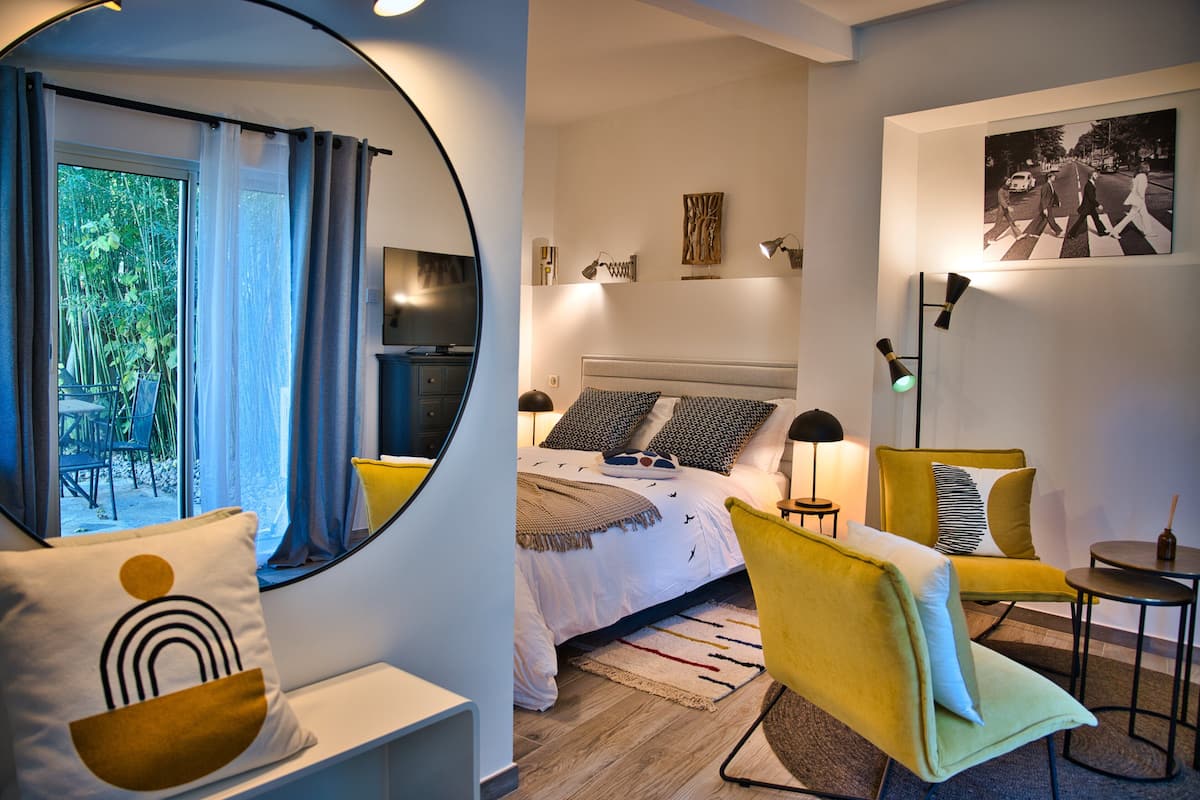 Quarto moderno com cama, mesas de cabeceira, uma cadeira, uma mesinha e um espelho.