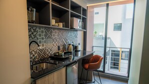 Et moderne køkken med et mønstret backsplash, indbygget ovn og kaffemaskine. Der er en bardisk med en stol og udsigt til det fri gennem et stort vindue.
