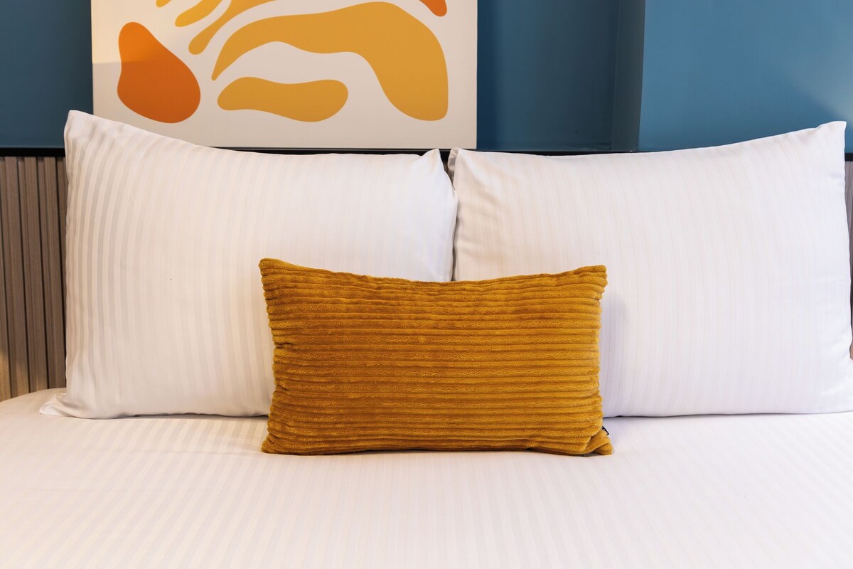 A bed with white pillows and a single mustard-colored pillow.